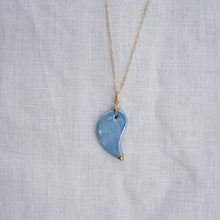 Load image into Gallery viewer, A gold chain necklace featuring a light blue, teardrop-shaped pendant with a polished gold tip, displayed on a textured white linen background.